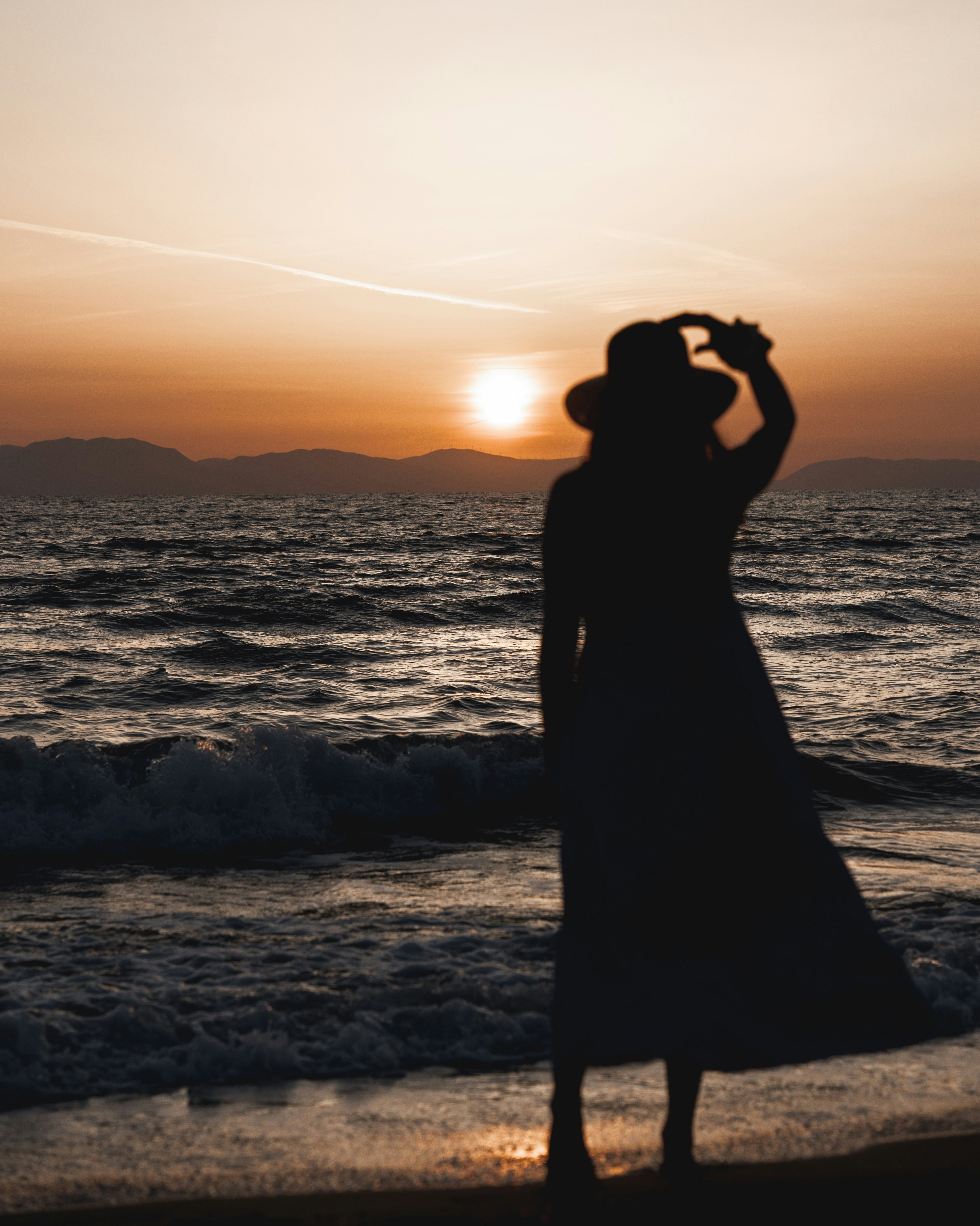 silhouette of woman standing on seashore during sunset